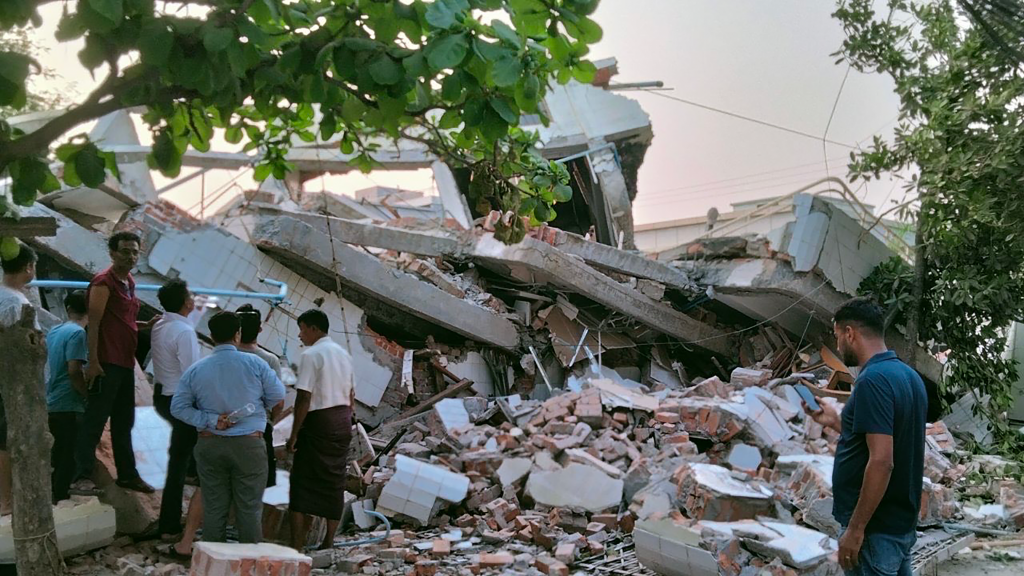 Een ingestort gebouw in Myanmar. Volledig ingestort, mensen kijken er verloren naar. 
